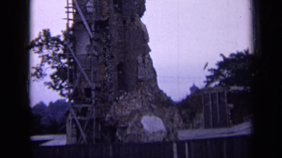 1963 Russia 8mm frame of a damaged masonry wall with scaffold poles, nearby foliage, and a wooden fence in the foreground.