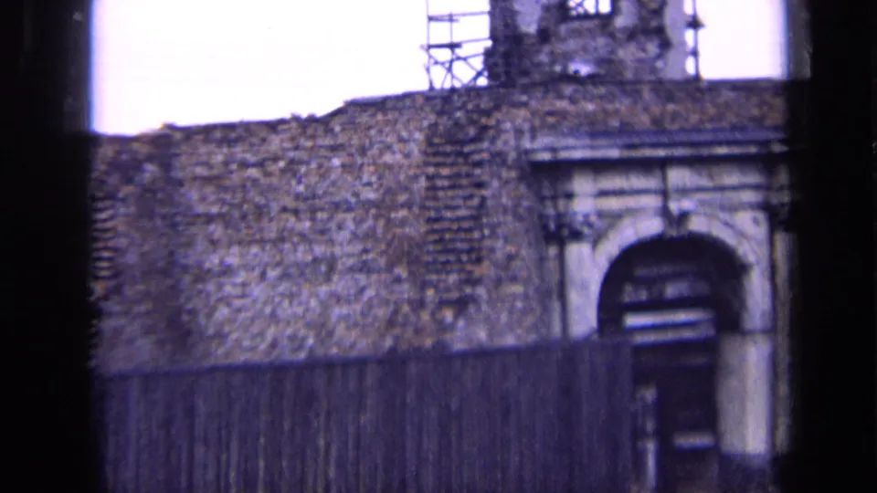 1963 Russia 8mm frame showing a stone wall, arched doorway, scaffolding above, and a wooden fence across the foreground.