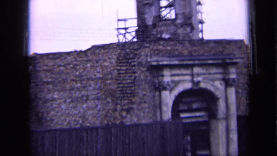 1963 Russia 8mm frame of a historic stone exterior with an arched doorway, scaffold platform, wooden fence, and dark framing at the sides.