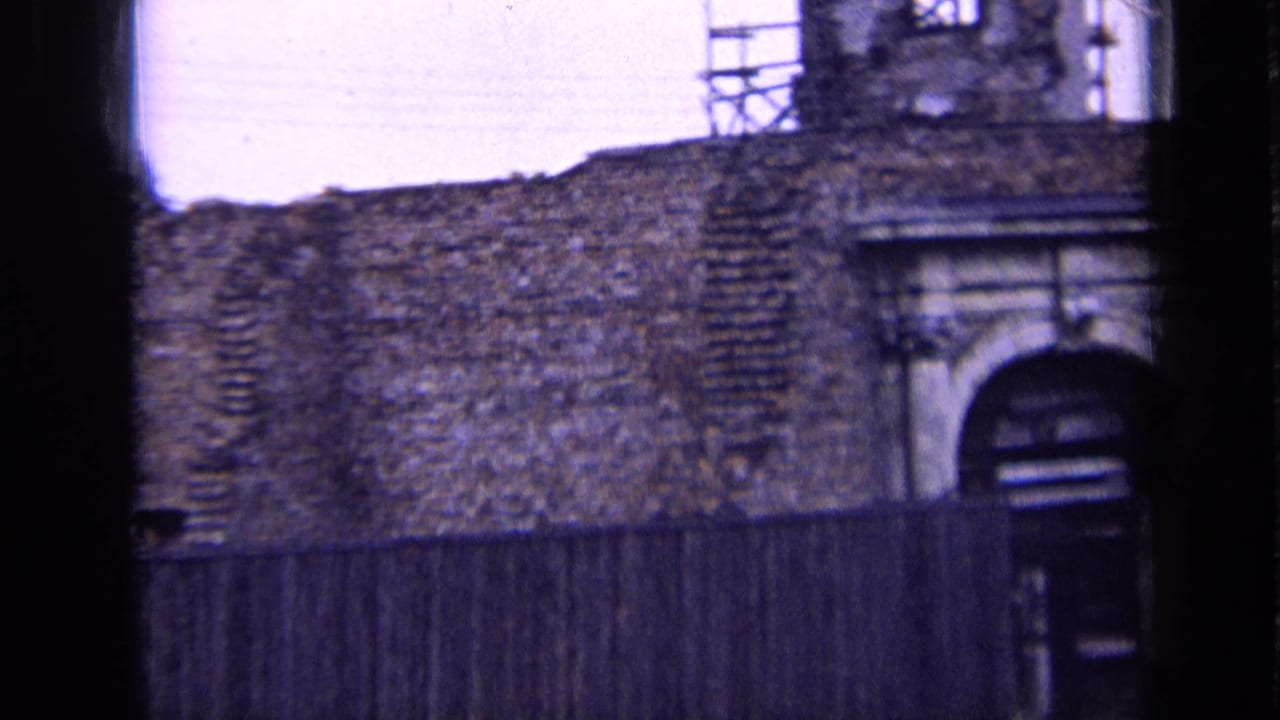 1963 Russia 8mm frame showing a weathered brick facade, arched stone doorway, timber fence, and scaffolding on the upper structure.