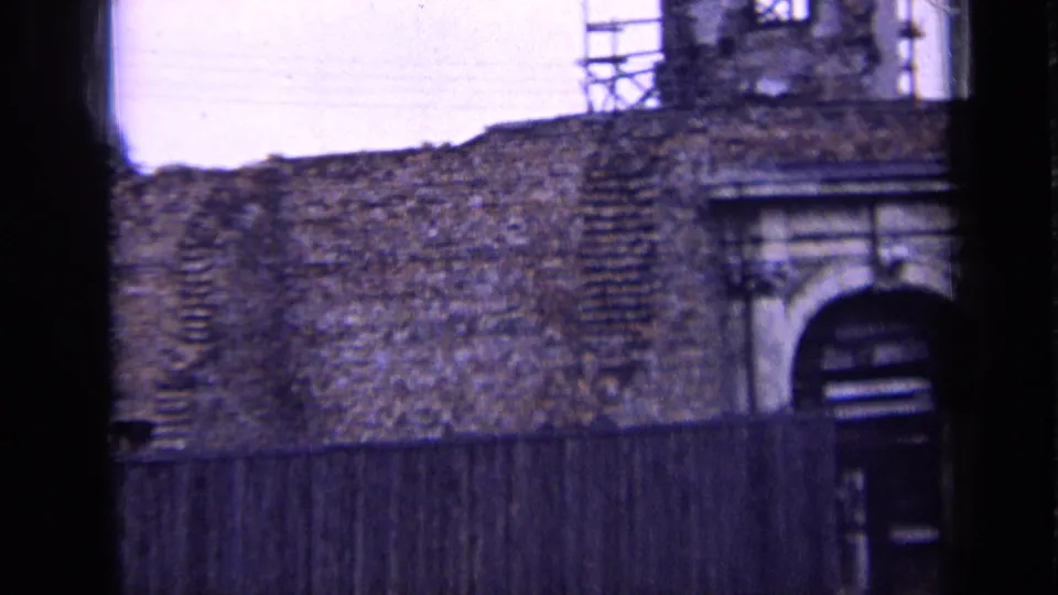 1963 Russia 8mm frame showing a weathered brick facade, arched stone doorway, timber fence, and scaffolding on the upper structure.