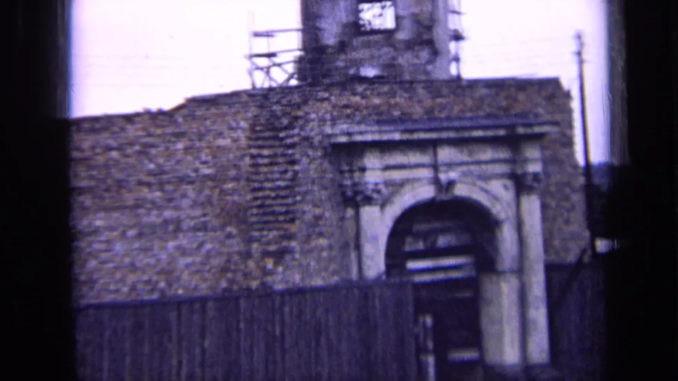 1963 Russia 8mm view of an old brick building with a stone-framed arched entrance, dark timber fence, and scaffolding above.