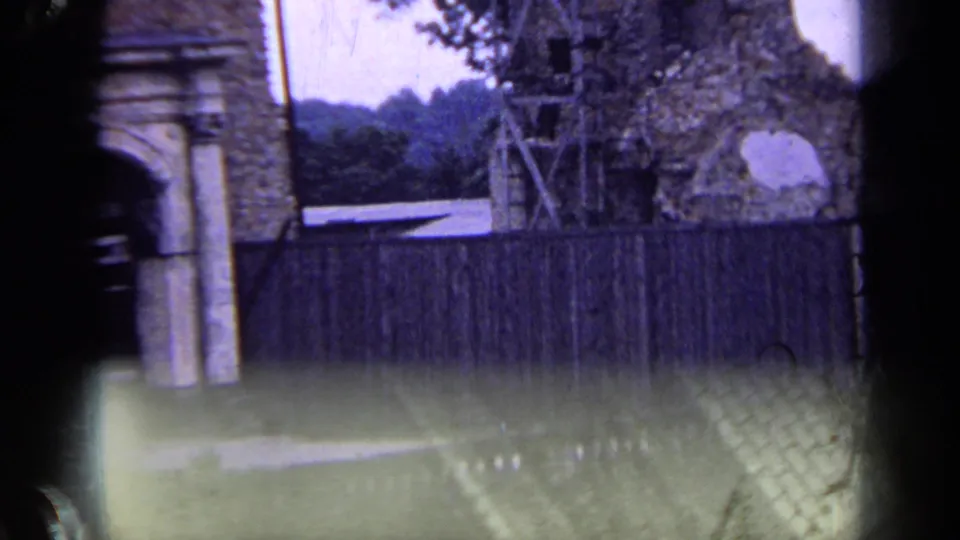 1963 Russia frame showing a fenced brick structure with scaffolding, an arched opening, nearby trees, and a distant wooded slope.