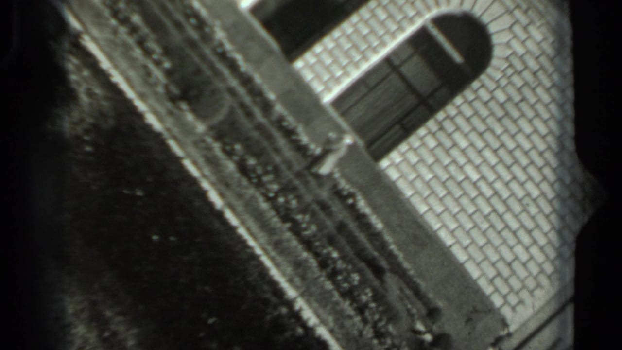 1963 Russian 8mm frame with a tilted view of a brick exterior, garden edge, and shadowed ground.