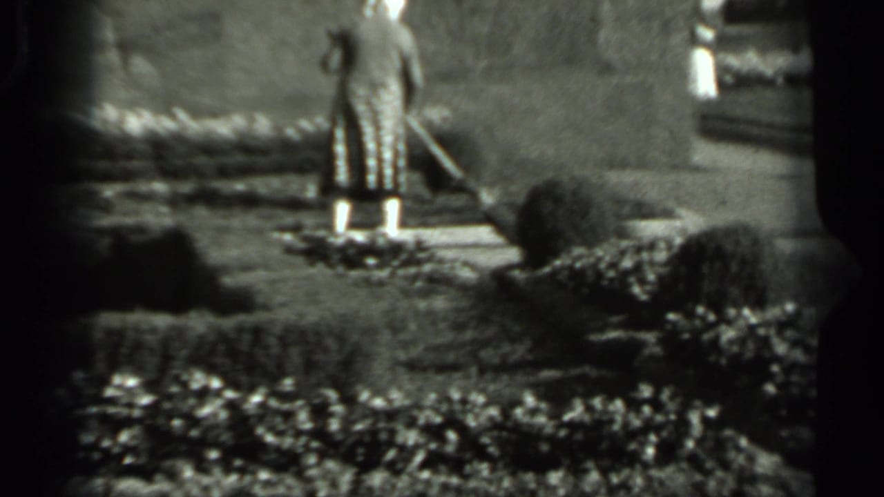 The woman pauses or turns with a broom on a garden path, with manicured hedges and a wall visible in the 1963 Russia footage.