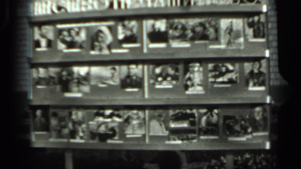 The final frame lingers on a wall-mounted grid of personal photographs, including portraits and small scene prints.
