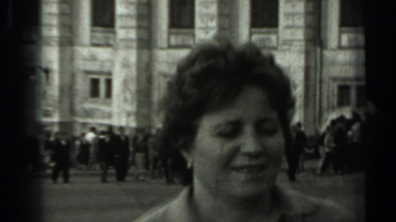 Woman smiling in the foreground with pedestrians and a stone building behind her.