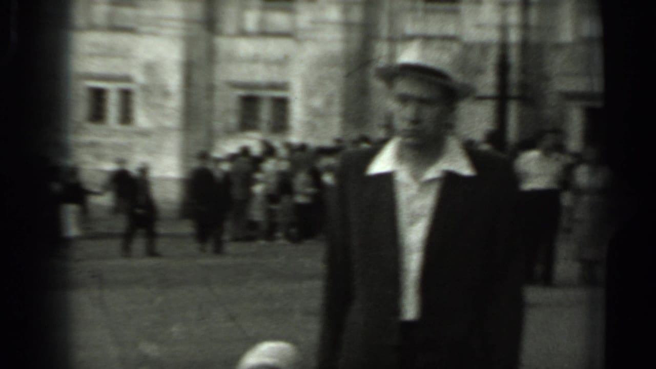A man in a brimmed hat and dark jacket passes through a Russian public square, with groups of pedestrians behind him.