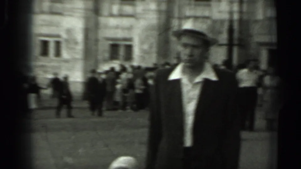 A man in a brimmed hat and dark jacket passes through a Russian public square, with groups of pedestrians behind him.