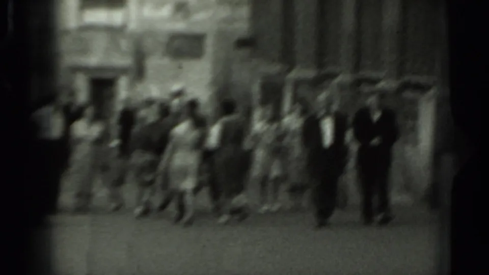 Soft-focus 8mm footage shows pedestrians crossing an open square in Russia, with the masonry building blurred behind them.