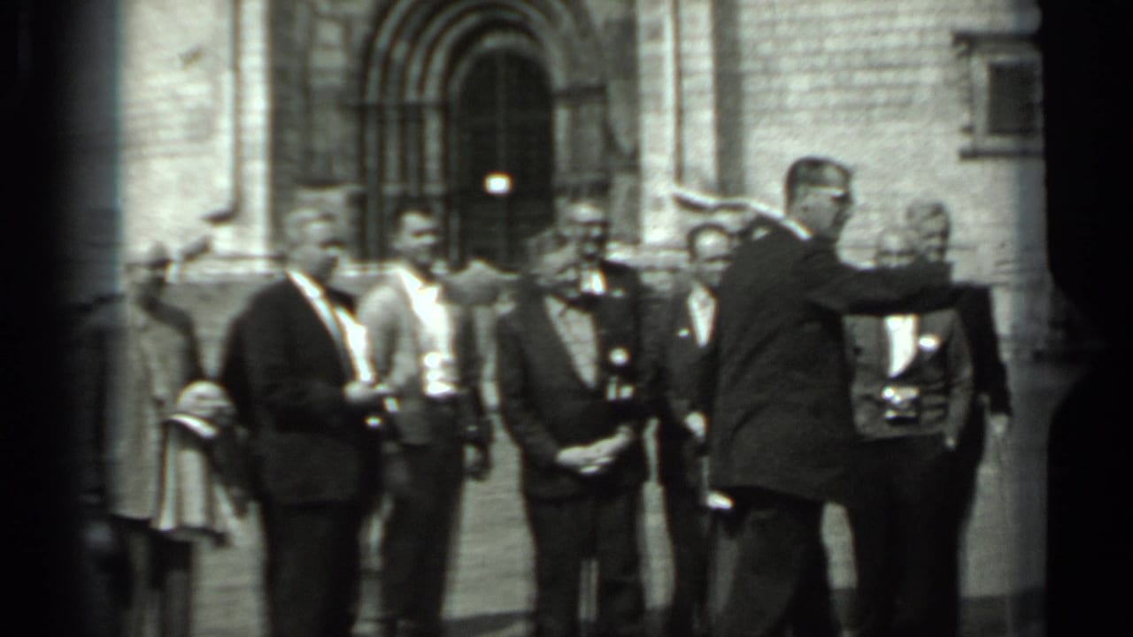 The group remains arranged in the courtyard, with suited men and a uniformed-looking figure near a stone arched entrance in Russia.