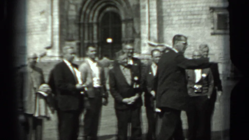 The group remains arranged in the courtyard, with suited men and a uniformed-looking figure near a stone arched entrance in Russia.