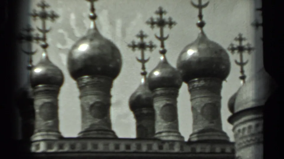 Close 8mm view of Russian cathedral onion domes, crosses, and a partial adjoining dome or tower at frame edge.