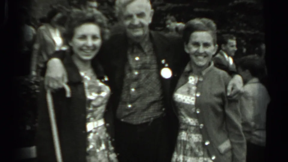 1963 Russia 8mm frame showing three adult visitors smiling together before domed architecture and a busy background.