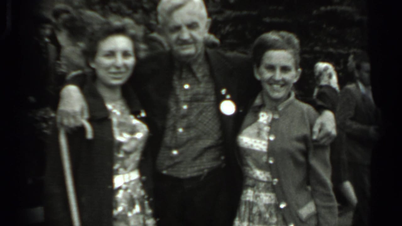 In 1963 Russia home-movie footage, an older man stands with his arms around two women as they smile in a crowded outdoor setting.