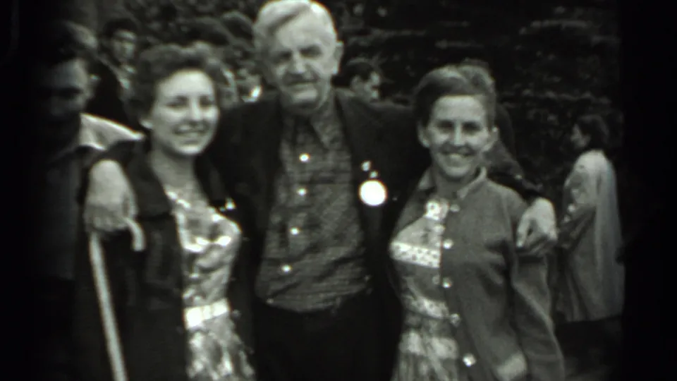 A posed 1963 Russia home-movie frame shows three adults smiling at the camera, with another person partly visible near the edge.