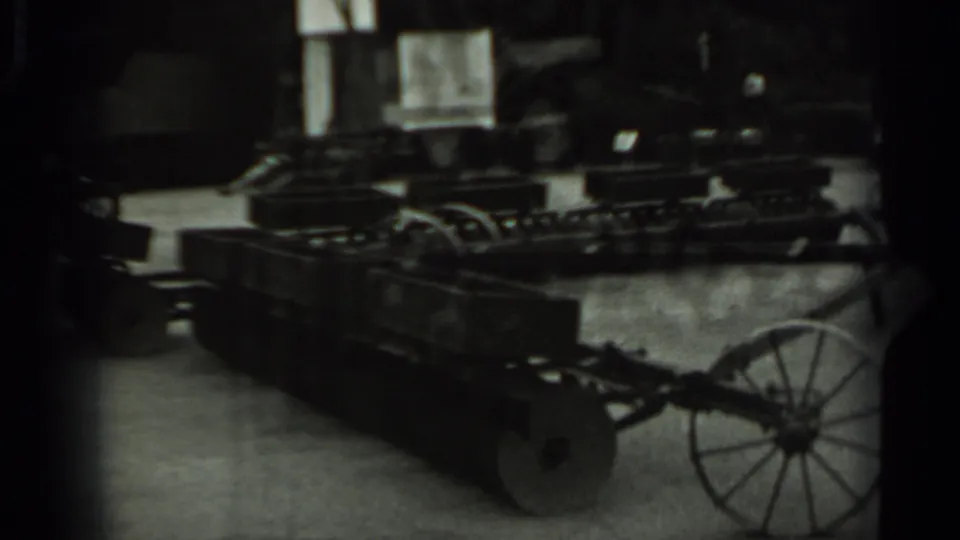 1963 Russia 8mm frame showing a long compartmented metal cart with spoked wheels stored indoors among other agricultural equipment.