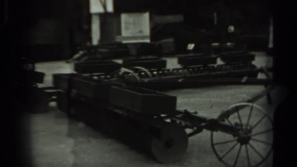 Soft 8mm frame of the same long wheeled metal cart in an indoor storage area, likely agricultural equipment based on clip metadata.