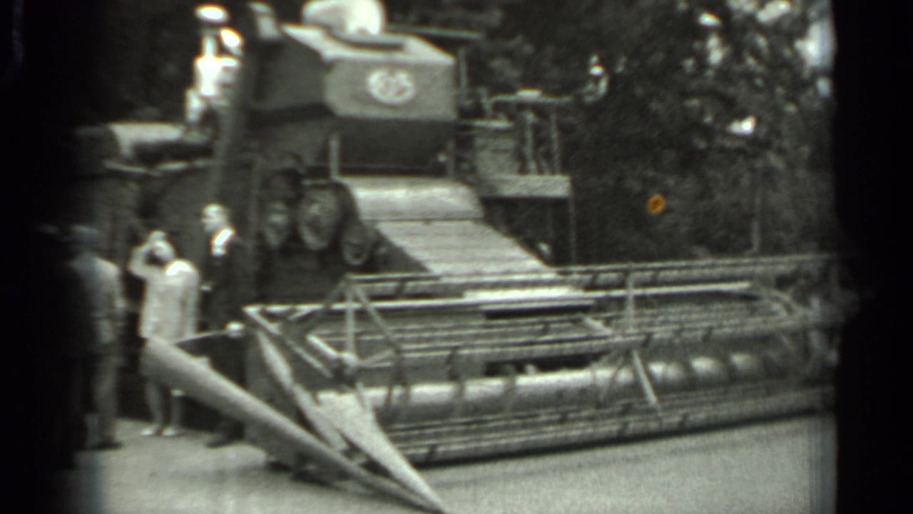 1963 Russia home-movie frame showing visitors near a large combine harvester, with its front cutting mechanism visible.