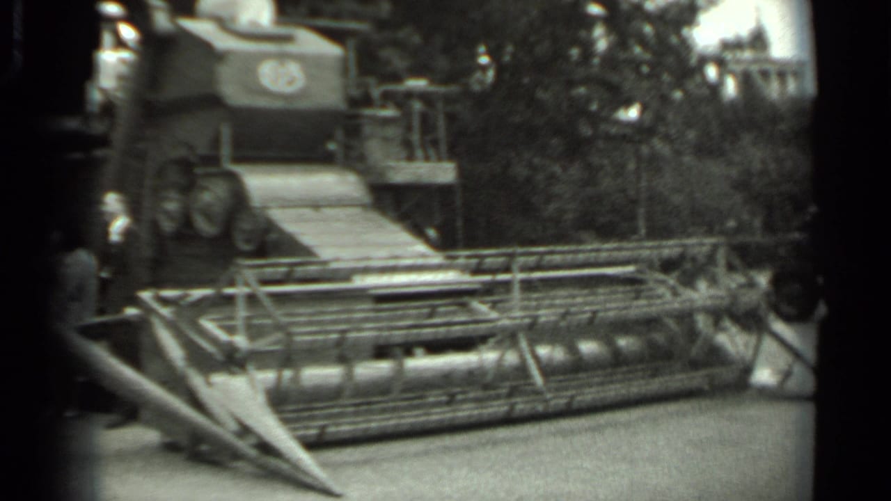 Black-and-white 8mm frame of a combine harvester display in Russia, with visitors partly visible near the front machinery.