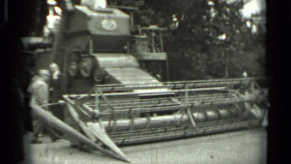 1963 Russia frame showing visitors close to the combine harvester's cutting header, with trees and display railings behind.