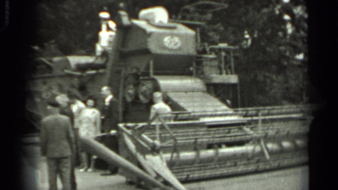 Men gather beside a large combine harvester with one man standing on its platform.
