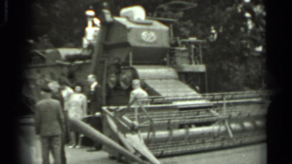 1963 Russia 8mm frame showing suited men inspecting a large combine harvester while a light-shirted man stands on the platform.