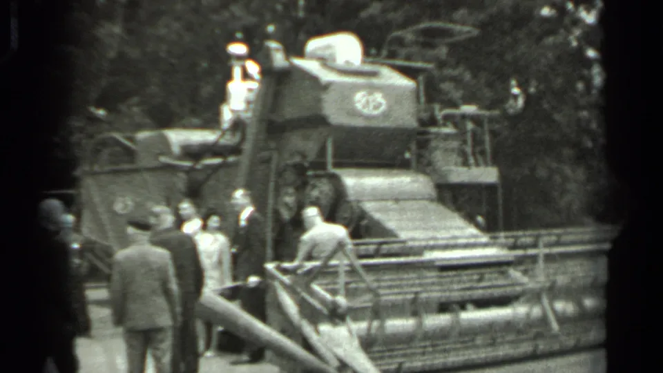 1963 Russia home-movie frame of several men gathered beside a large combine harvester, with one person elevated near the controls.