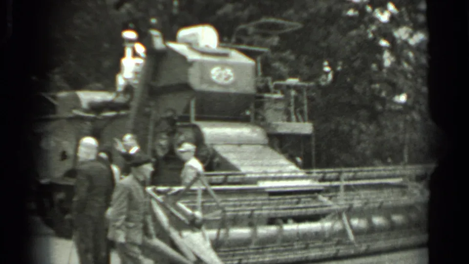 1963 Russia 8mm frame with visitors standing near the front cutting assembly of a large combine harvester at an outdoor exhibition area.
