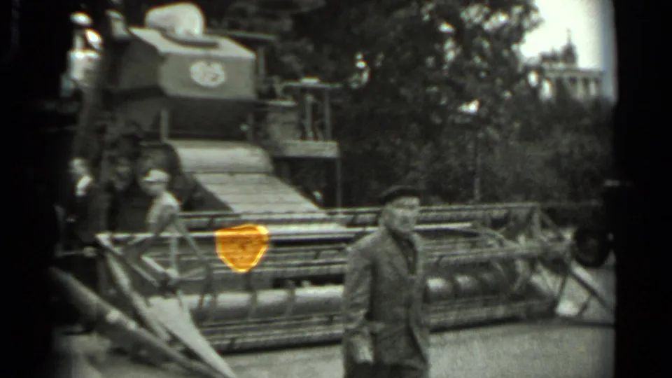 1963 Russia 8mm frame with a man in the foreground and a large combine harvester behind him, with trees and a distant building visible.
