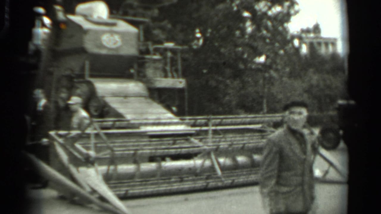 1963 Russia 8mm frame showing men near a large tracked harvester on outdoor display, with trees behind the machine.