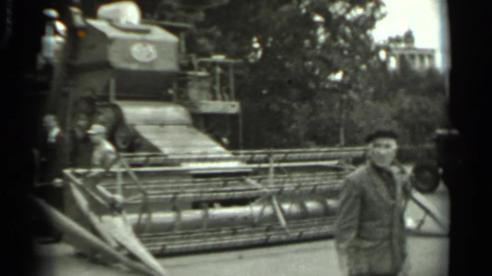 1963 Russia 8mm frame showing men near a large tracked harvester on outdoor display, with trees behind the machine.