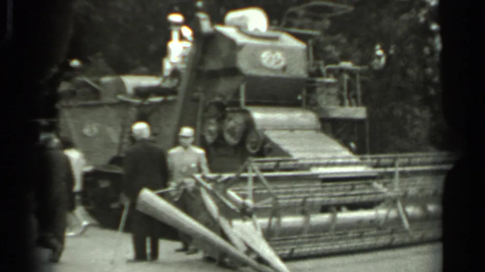 1963 Russia 8mm frame showing visitors in dark coats around a large agricultural harvester on display.