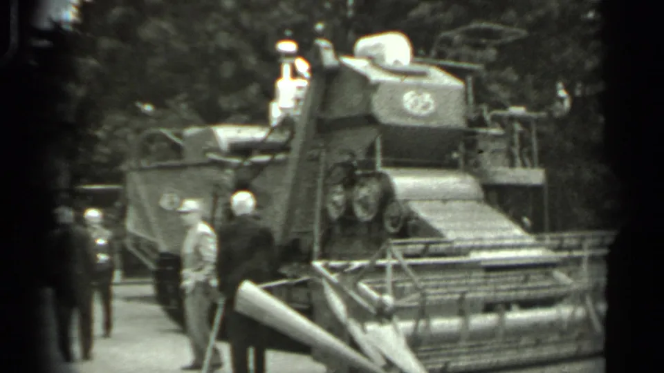 1963 Russia home-movie frame showing men in suits near a large tracked agricultural machine at an apparent exhibition.