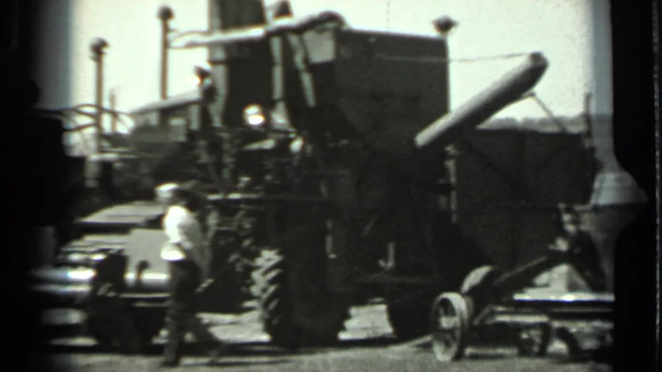 1963 Russia 8mm frame showing a worker walking beside large agricultural machinery in a bright outdoor rural setting.