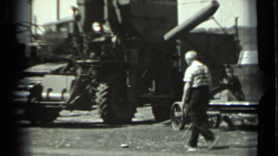 1963 Russia 8mm frame of a worker walking alongside a large wheeled farm machine with exposed mechanical components.