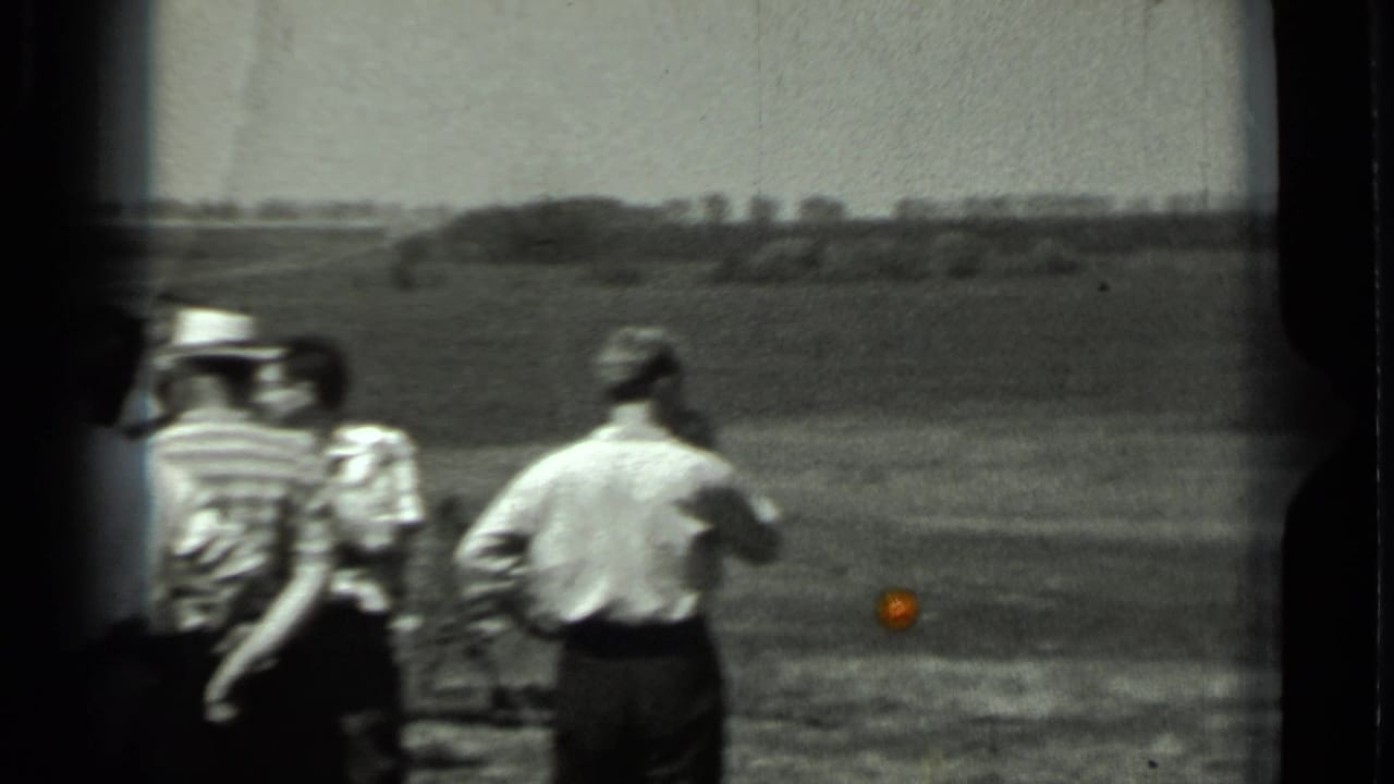 1963 Russia 8mm frame showing adult men in casual shirts and hats standing in a rural field near equipment out of frame.
