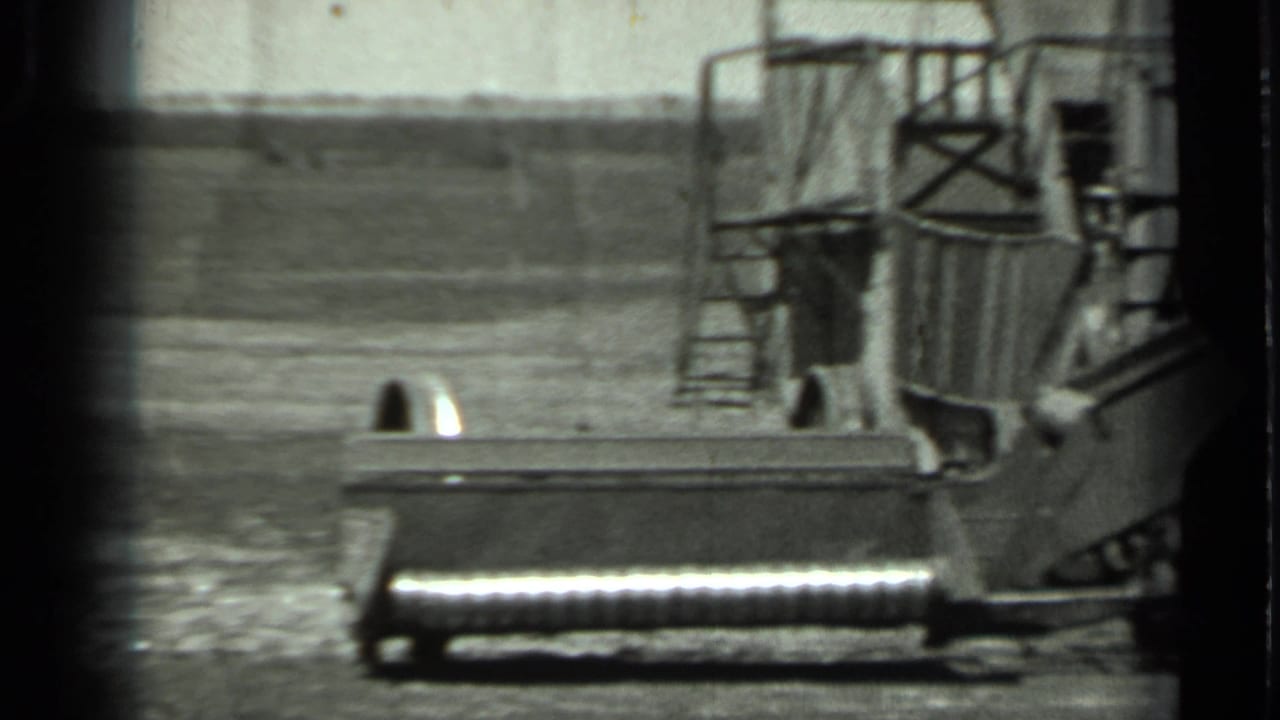 A large tracked machine sits in an open field with railings and a ladder visible.