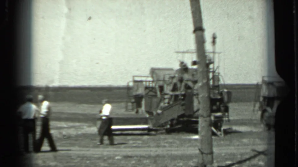 1963 Russia 8mm frame showing adult men near a large tracked vehicle or equipment platform in a rural setting.
