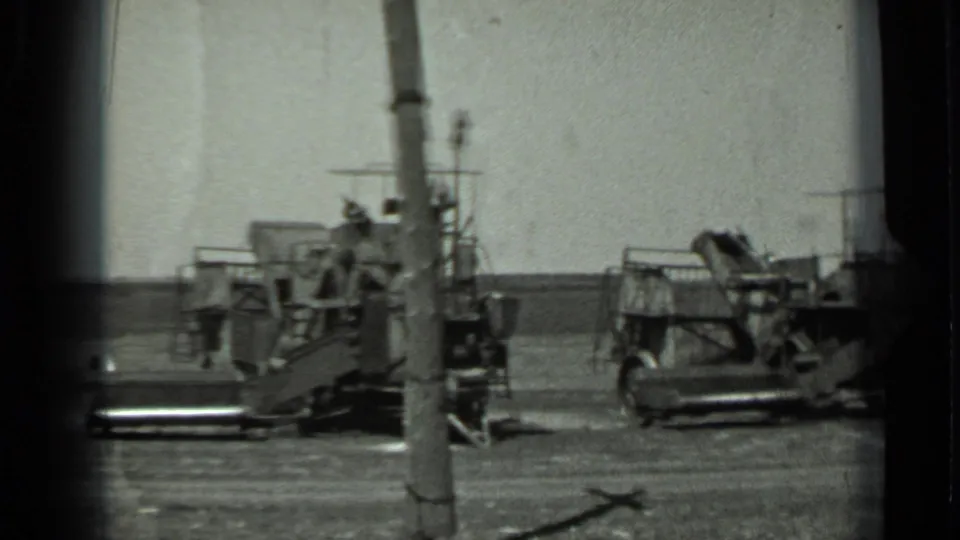1963 Russia 8mm frame showing tracked equipment, a platform, and a pole in an open field, with people partly visible near the machinery.