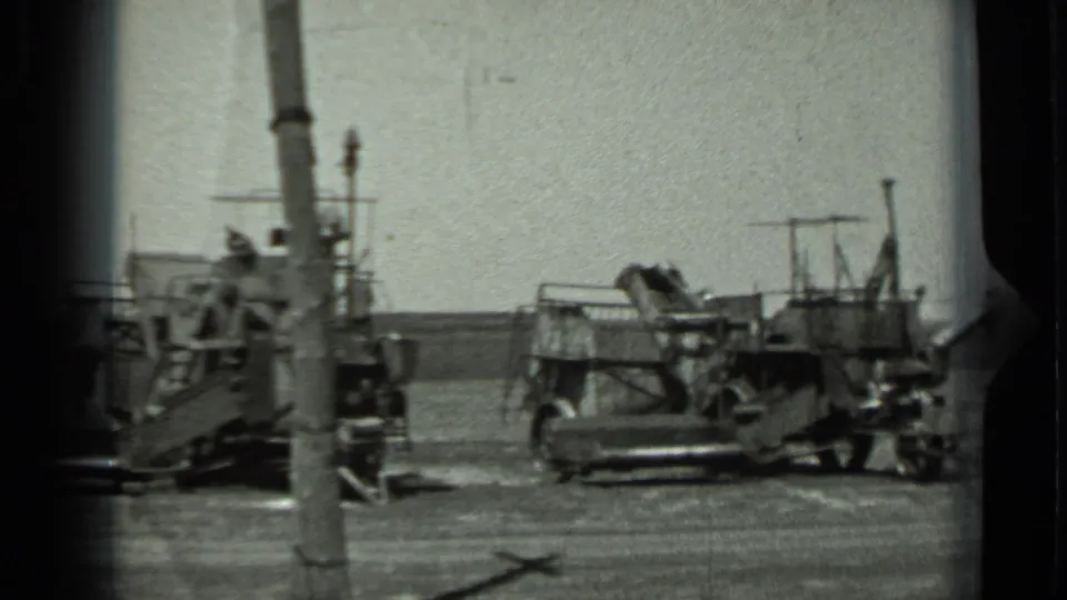 1963 Russia 8mm frame showing parked military-looking vehicles on flat open ground, partly obscured by a utility pole.