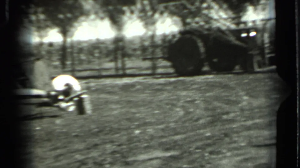 Grainy 1963 Russia frame showing field machinery, a dark tractor-like vehicle, trees, and uneven home-movie exposure.
