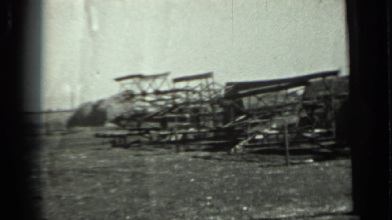 1963 Russia 8mm frame showing a dim outdoor area with indistinct low structures or stacked material and open ground.