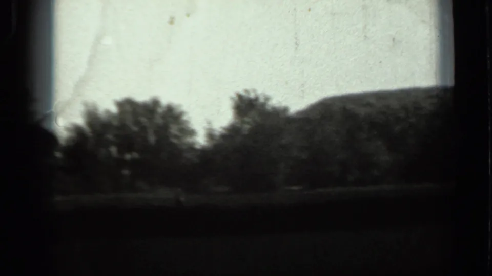 1963 Russia 8mm frame showing a dim landscape with trees, open ground, and a low hill in the distance.