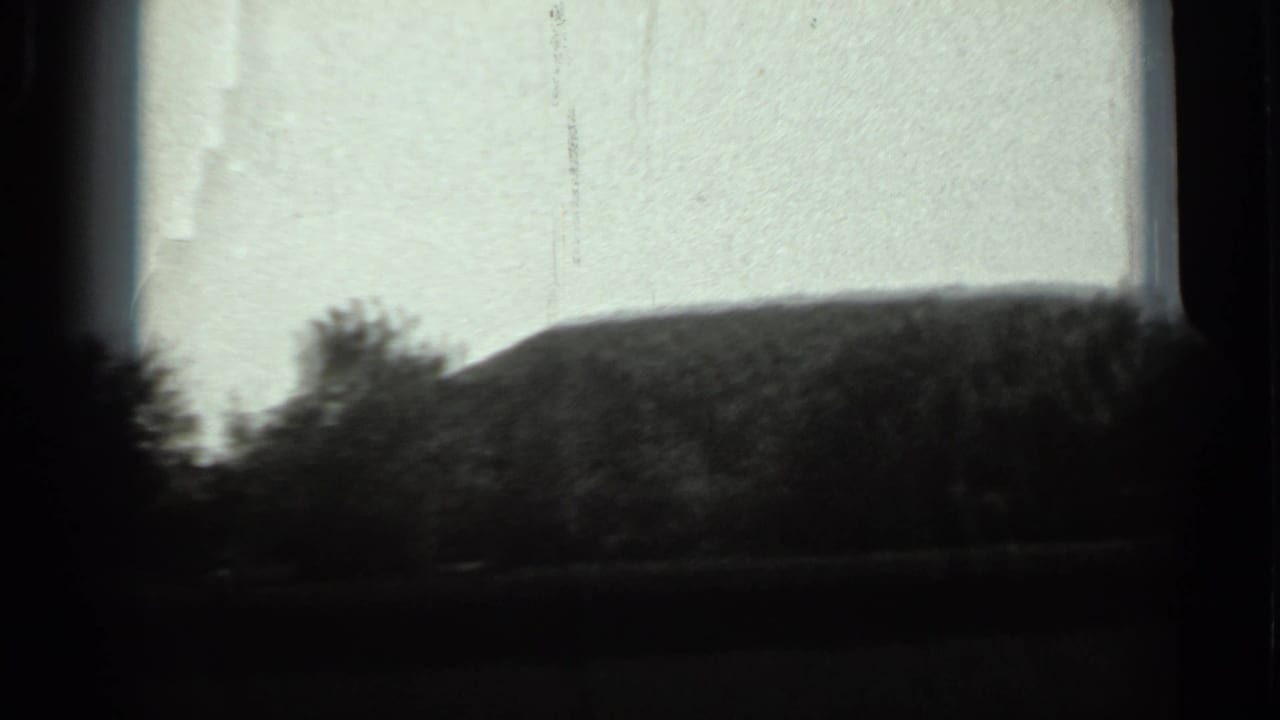 1963 Russia 8mm frame showing a dark tree line and low dirt mound against a pale sky, partly bordered by dark frame edges.