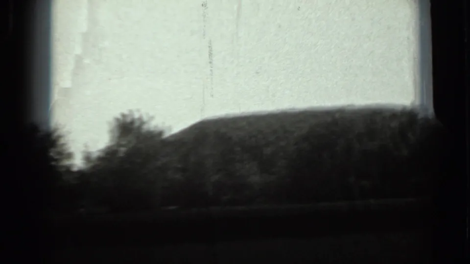 1963 Russia 8mm frame showing a dark tree line and low dirt mound against a pale sky, partly bordered by dark frame edges.
