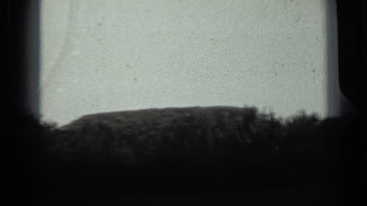 1963 Russia 8mm frame with a low mound and shrub silhouettes under a washed, pale sky with visible film wear.