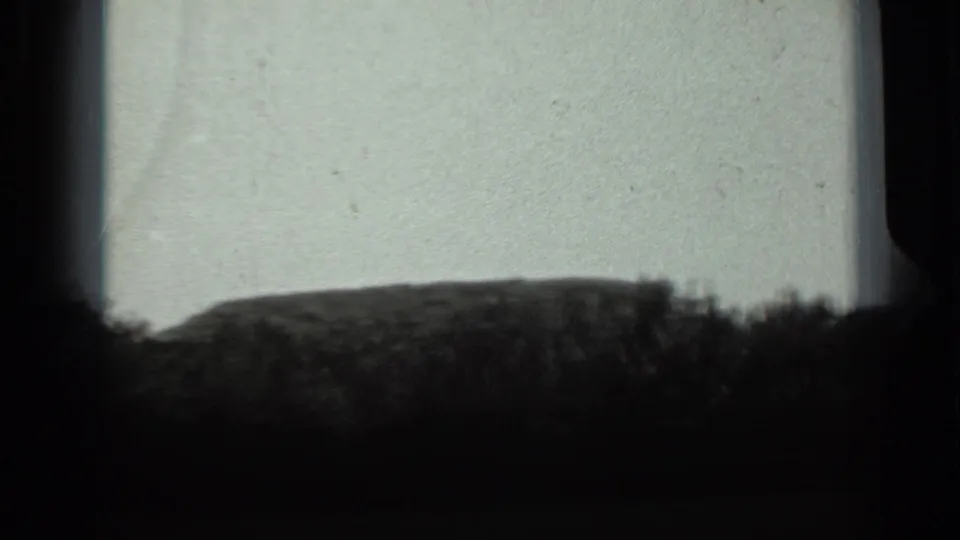 1963 Russia 8mm frame with a low mound and shrub silhouettes under a washed, pale sky with visible film wear.