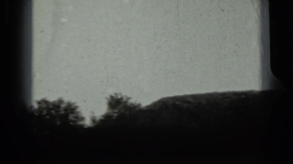 1963 Russia 8mm frame showing tree silhouettes and a low mound through dark borders, with soft focus and visible grain.