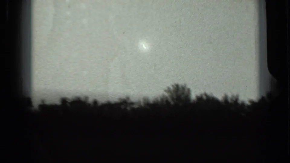 Soft black-and-white home-movie frame showing sky, tree silhouettes, and the dark edges of the 8mm film gate.